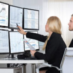 Financial workers analyzing data displayed on computer screens at desk in office.