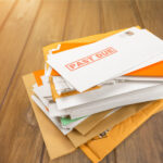 Pile of envelopes with overdue utility bills isolated on white.