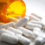 A prescription bottle on its side with several white pills spilling out.