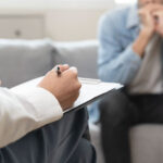 A therapist takes notes while a client, sitting on a couch, appears to be in distress during a counseling session.